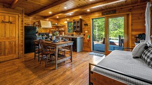 Ein Holzblockhaus mit Küche, Essbereich und einem Bett.