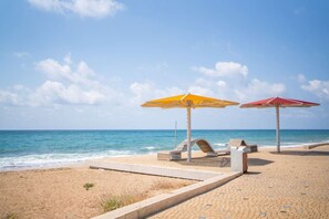 A beach with two umbrellas, a wooden bench, and a concrete walkway. - Tranquil Stay Near Beach by Sea N' Rent (Nahariya)