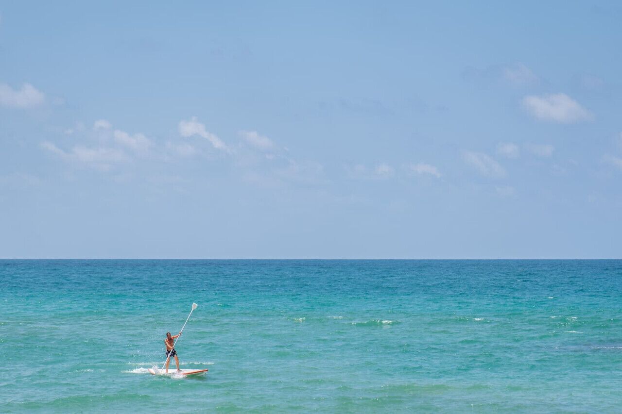 A person paddleboarding on a calm sea with a clear sky.