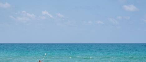 A person paddleboarding on a calm sea with a clear sky.