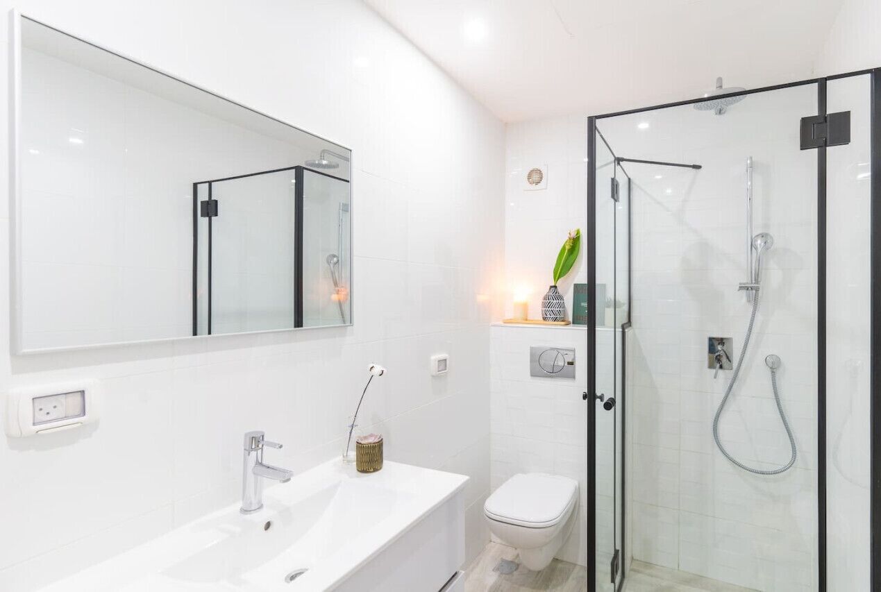 A modern bathroom with a glass-enclosed shower, a white sink with a mirror, and a toilet.