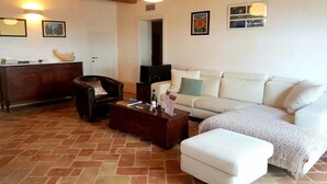 A living room with a sofa, a coffee table, a chair, and a fireplace. There are pictures on the wall and a door in the background. - Manor in Marche with Pool and Adriatic Views (Monsano)