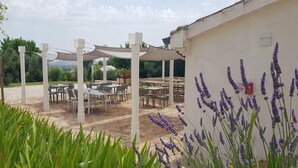 An outdoor patio with tables and chairs, surrounded by greenery and lavender plants. - Manor in Marche with Pool and Adriatic Views (Monsano)