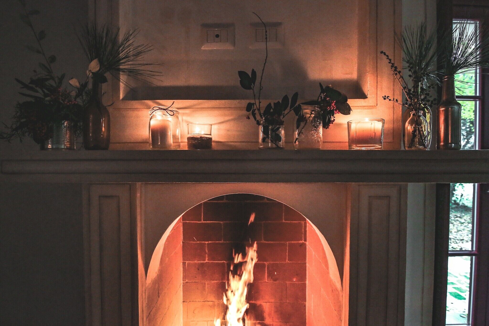 A fireplace with a burning fire, surrounded by decorative vases and candles on a mantel.