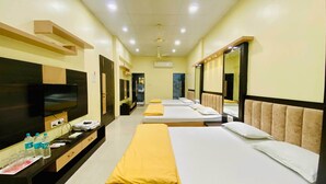 A hotel room with three beds, a TV, a desk with a mirror, and a bathroom visible through an open door. - Hotel Panchavati Palace (Khandwa)