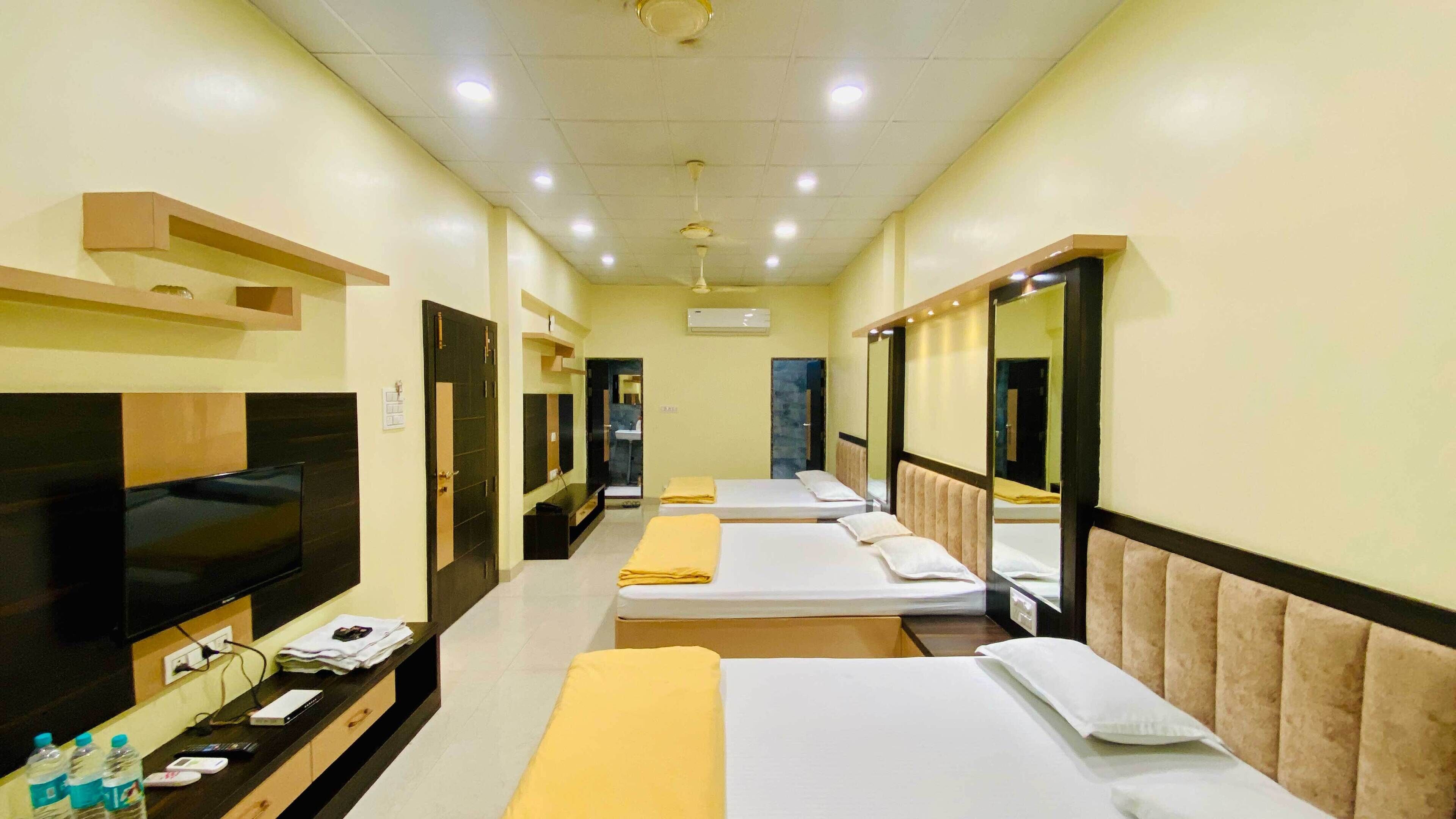 A hotel room with three beds, a TV, a desk with a computer, and a mirror.
