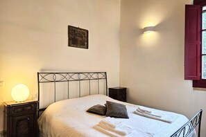 Un lit bien fait, avec des oreillers et une serviette pliée, une lampe de chevet, une petite table et un tableau accroché au mur.