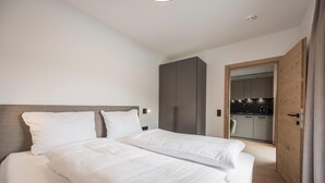 A modern bedroom with a large bed, a wardrobe, and a kitchen area visible through an open door. - Apartment in Kirchberg near Schaterzlift (Kirchberg in Tirol)