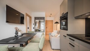 A modern kitchen with a built-in oven, a dining area with a table and chairs, and a living area with a sofa. - Apartment in Kirchberg near Schaterzlift (Kirchberg in Tirol)