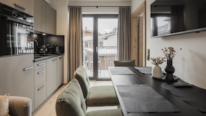 A modern kitchen with a built-in oven, a dining area with a table and chairs, and a view of the city through large windows. - Apartment in Kirchberg near Schaterzlift (Kirchberg in Tirol)