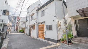 Una calle residencial estrecha flanqueada por casas, con una puerta de madera en el centro, plantas en macetas y cables eléctricos a la vista.