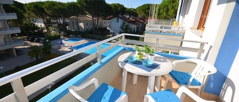 A balcony with a pool, white chairs, and a table with potted plants.