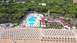 An aerial view of a beach resort with multiple swimming pools, sun loungers, and a large sandy beach area. - Spacious villa in Lignano (Lignano Sabbiadoro)