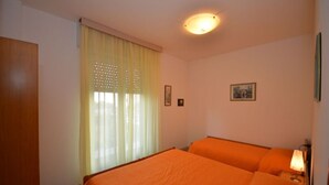 Una habitación con dos camas, una ventana con cortinas, una lámpara de techo y un cuadro en la pared.
