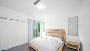 Quarto com cama, mesa de cabeceira, porta de correr de vidro e janela com persianas.