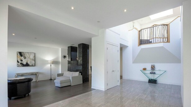 Uma sala de estar ampla, com design moderno, apresentando um sofá branco grande, uma poltrona preta e uma mesa de centro de vidro.