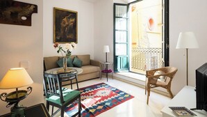 Ein Wohnzimmer mit einer Couch, einem Esstisch, einem Stuhl, einer Lampe, einem Gemälde und Blick auf einen Balkon.