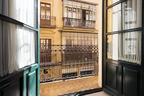 Blick durch ein Fenster mit einem Metallbalkonläufer, einem Backboden und einem Gebäude mit mehreren Fenstern und Balkonen im Hintergrund.