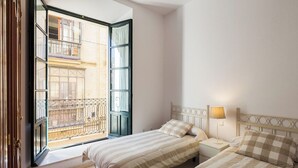 Ein Schlafzimmer mit zwei Betten, einem Fenster mit Blick auf ein Gebäude und einem Nachttisch mit Lampe.