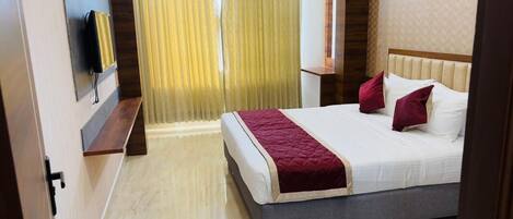 A hotel room with a bed, a TV mounted on the wall, a bedside table, and a window with curtains.