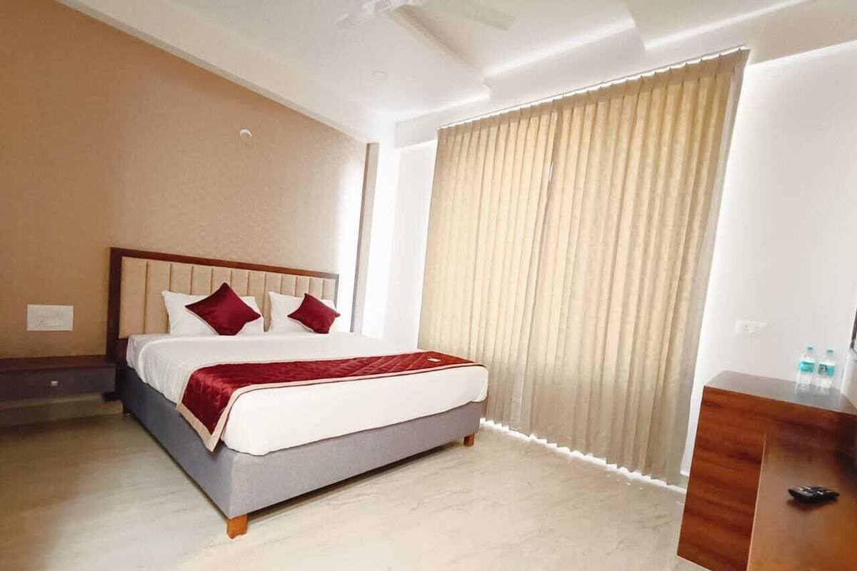 A hotel room with a bed, a wooden dresser, and a window with curtains.