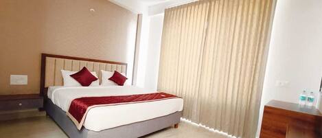 A hotel room with a bed, a wooden dresser, and a window with curtains.