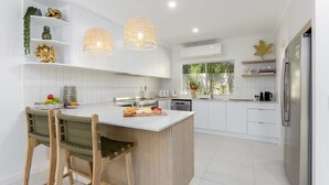 A modern kitchen with white cabinetry, a central island, a built-in stove, and a refrigerator. - Sorrento Breeze | Port Douglas (PORT DOUGLAS)