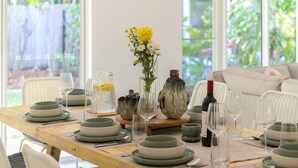 A dining table set with green plates, clear glasses, and a vase with yellow flowers. - Sorrento Breeze | Port Douglas (PORT DOUGLAS)