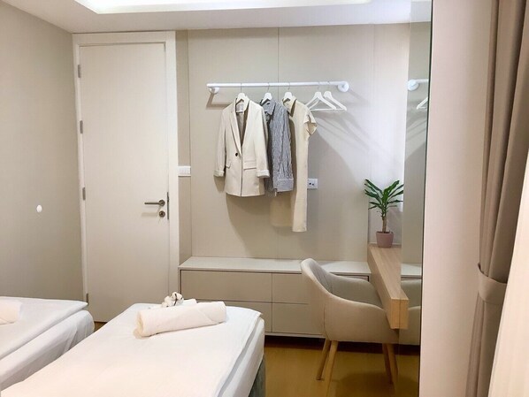 A hotel room with two beds, a desk, a chair, a wardrobe, and a hanging clothes rack.