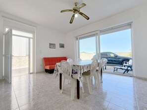 A dining area with a table and chairs, a ceiling fan, and large windows with a view of a car and landscape.