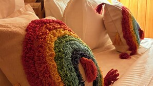 Ein Bett mit farbenfroher Decke und Kissen, einem hölzernen Kopfteil und einer Lampe im Hintergrund.