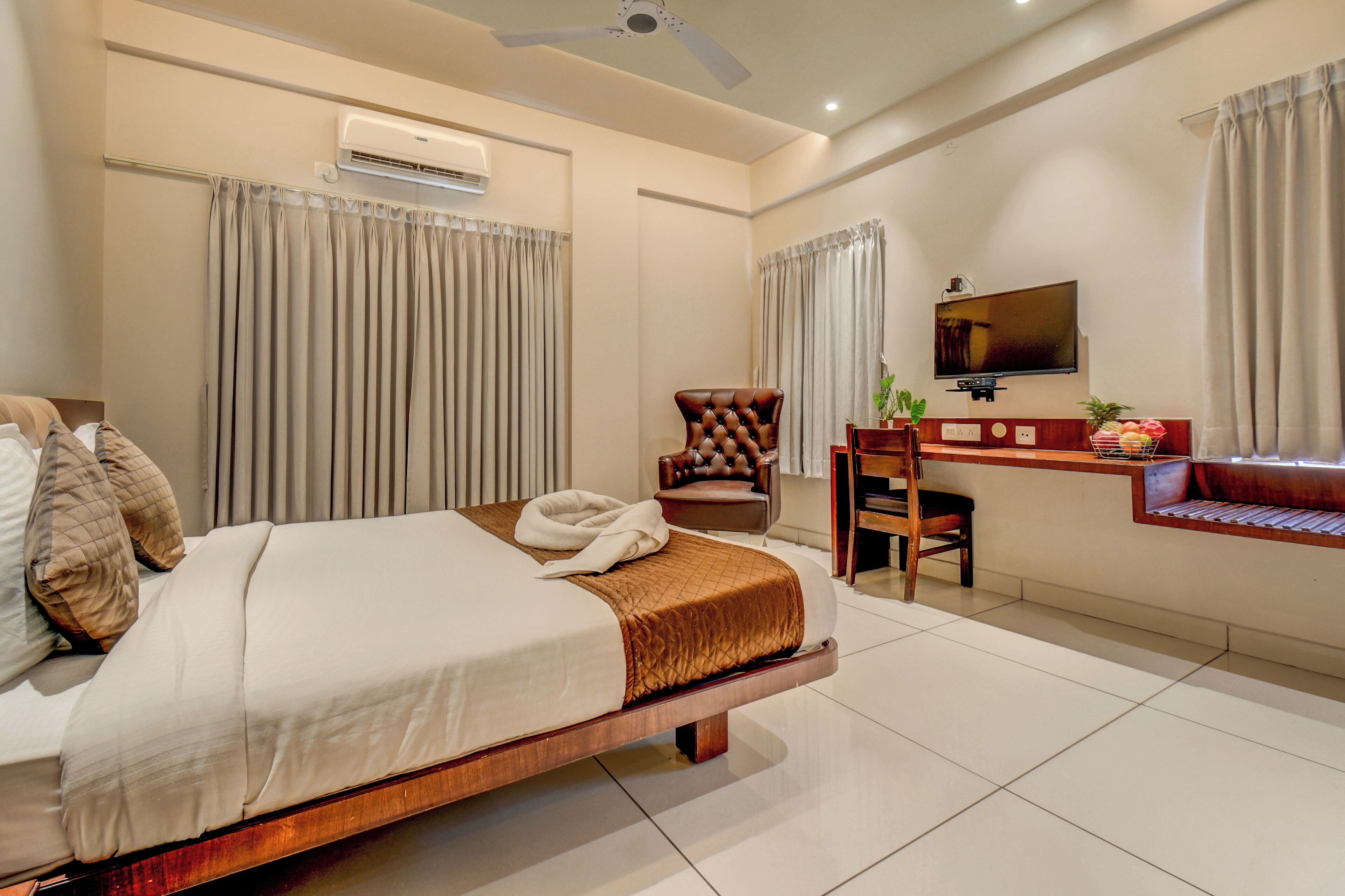 A hotel room with a bed, a desk, a chair, a television, and an air conditioning unit.