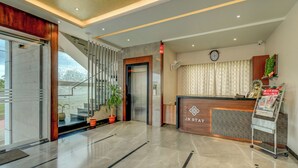 Ein Hotel-Empfangsbereich mit modernem Design, einschließlich einer Rezeption, einer Uhr und einer Treppe zu den oberen Etagen.