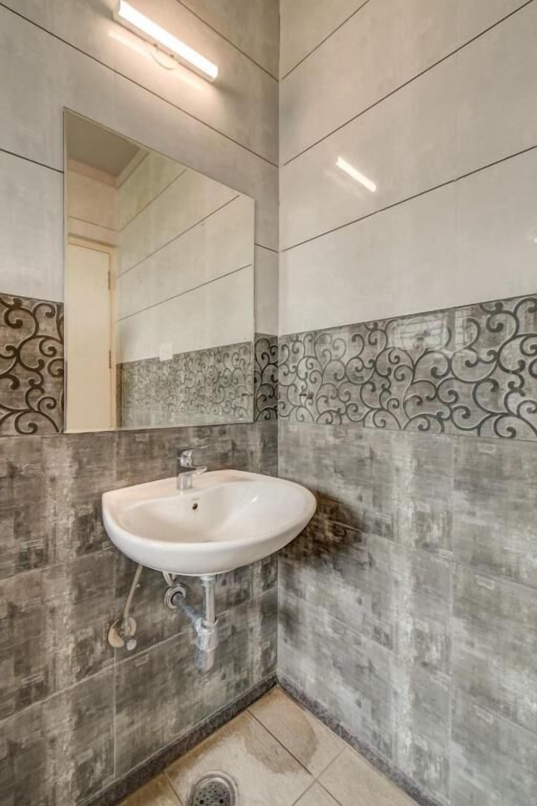 Un baño con un lavamanos blanco, un espejo y azulejos decorativos en las paredes.