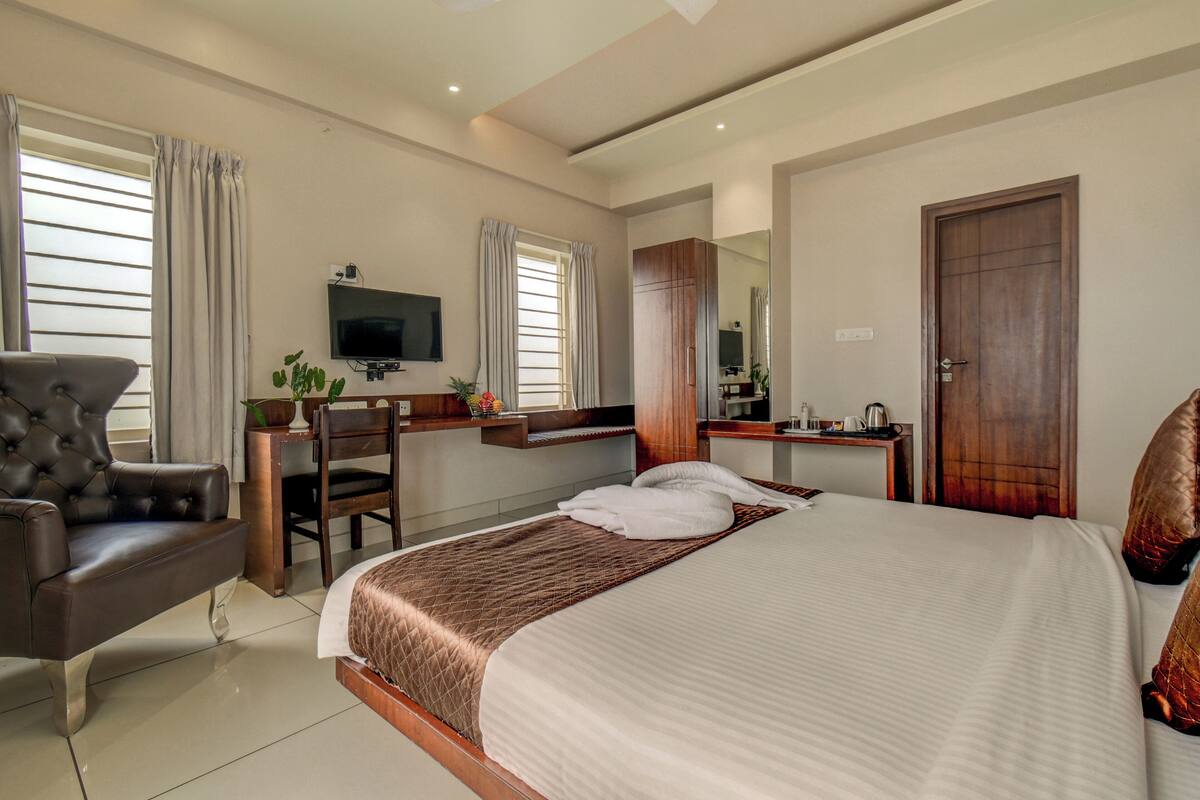 A hotel room with a large bed, a desk with a chair, a television, and a wardrobe.