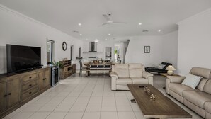 Un salon moderne doté d’un téléviseur à écran plat, d’un coin repas avec une table et des chaises, d’un canapé et d’un ventilateur de plafond.