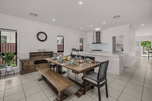 A modern kitchen with a dining area, white cabinetry, and a large window.