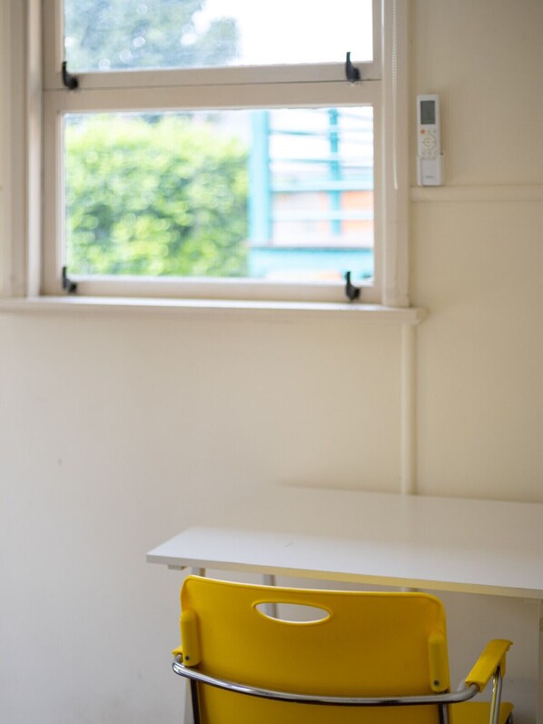 A room with a window, a yellow chair, and a white table.