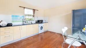 Una cocina compacta con lavadora, una mesa de vidrio y un ventanal con cortinas.