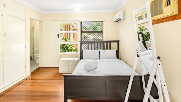 A bedroom with a bed, bedside table, and a window with a view of greenery. - Affordable Studio – Steps from UQ/ Shops/ Transit (Saint Lucia)