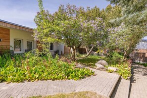 Un jardin avec un chemin pavé, des arbres en fleurs et un bâtiment moderne doté de grandes fenêtres.
