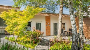 Un bâtiment moderne doté d’une porte en bois, d’un chemin pavé et d’un espace jardin agrémenté d’arbres et de plantes.