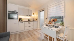 Une cuisine compacte avec des meubles blancs, un four encastré et un coin repas comprenant une table et des chaises blanches.