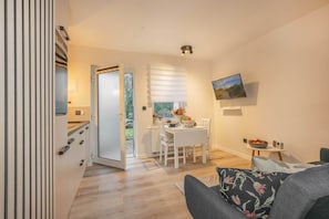 A modern kitchen with white cabinets, a dining area with a table and chairs, a TV mounted on the wall, and a view of the outdoors through a door. - Modern vacation apartment with terrace not far from the Baltic Sea (Benz)
