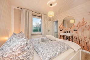 Een slaapkamer met een bed, nachtkastje, spiegel en een raam met gordijnen.