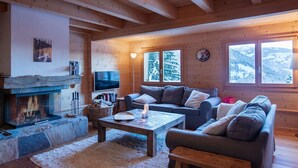 A cozy log cabin interior with a fireplace, a sofa set, a television, and large windows with a snowy mountain view. - Wonderful private villa for 8 guests with terrace (Alpe Des Chaux)