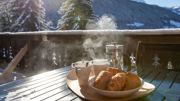 A table with a tray of croissants and a cup of coffee, steam rising from the coffee, set against a snowy mountain backdrop. - Wonderful private villa for 8 guests with terrace (Alpe Des Chaux)
