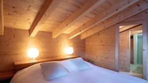 A wooden cabin bedroom with a bed, two wall-mounted lights, and a glass door leading to a bathroom. - Wonderful private villa for 8 guests with terrace (Alpe Des Chaux)