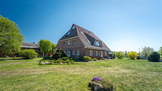 A large, two-story house with a sloped roof, a well-maintained lawn, and a small garden area with shrubs and a rock. - Dascha vacation apartment in the Baltic seaside resort of Dierhagen (Dierhagen)