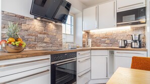 A modern kitchen with white cabinets, a stone backsplash, a microwave, an oven, and a coffee maker. - Dascha vacation apartment in the Baltic seaside resort of Dierhagen (Dierhagen)